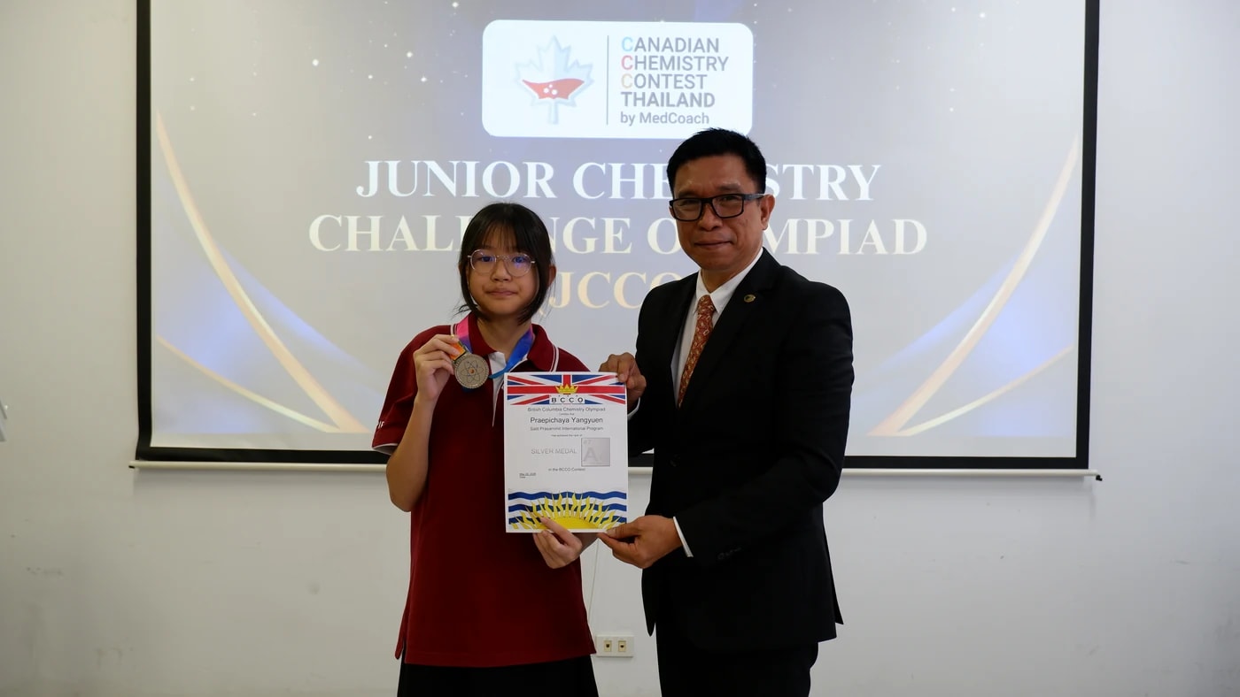 ผู้ได้รับเหรียญเงินพร้อมใบประกาศนียบัตร JCCO แสดงด้านหลังเหรียญสัญลักษณ์อะตอม